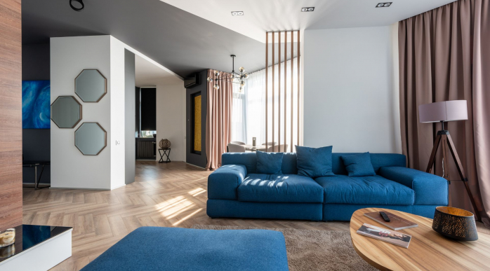 Salon moderne et lumineux au design contemporain, avec canapé bleu, parquet en chevron et grandes baies vitrées laissant entrer la lumière naturelle.