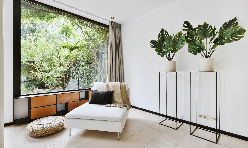 On aperçoit un petit salon très épurée il y a un petit pouf blanc avec des plantes, on observe une grande télé, l'ambiance est très reposante