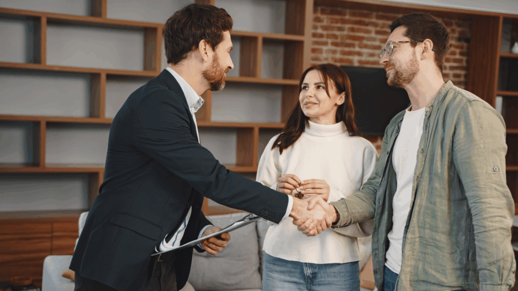 On aperçoit un agent immobilier qui sert la main ç un homme qui est avec sa conjointe
