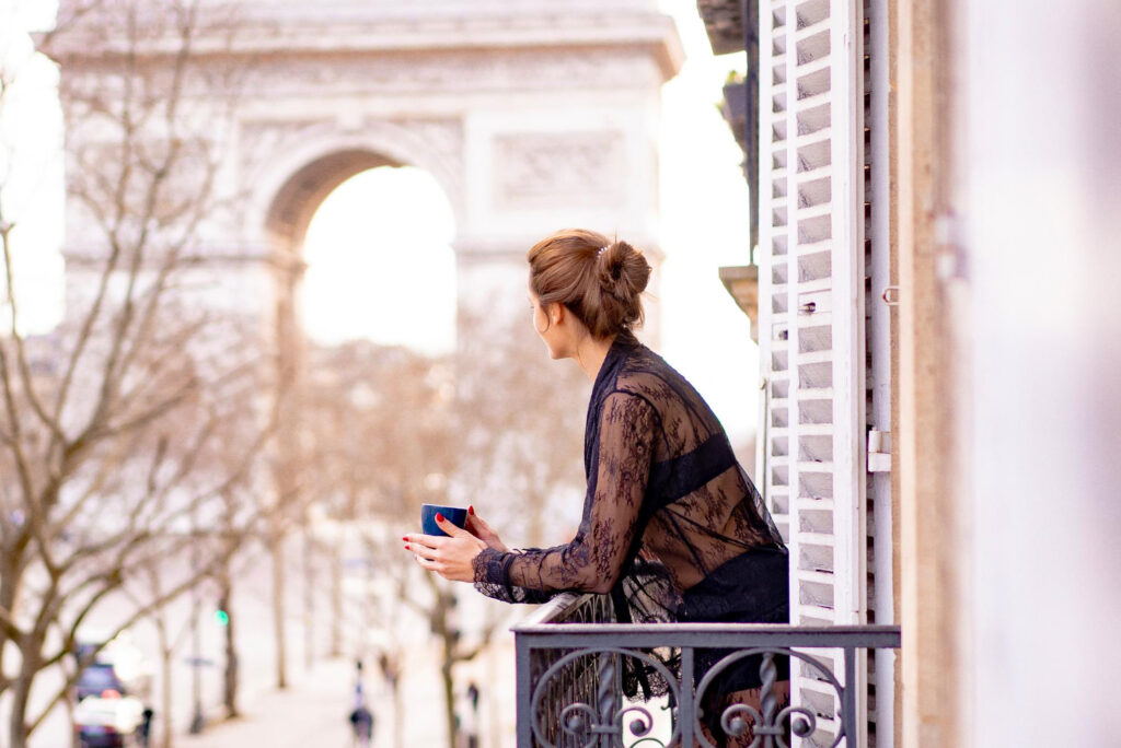 Jolie femme yang en pyjama boit du café sur le balcon le matin dans la ville de Paris. vue sur l'arc de triomphe.
