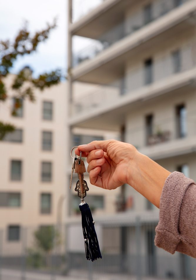 Main tenant une clé d'appartement avec en fond la vue sur un appartement